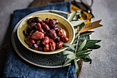 Bowl of bright Greek olives, accompanied by a sprig of fresh olive leaves, in a blue napkin, with a label labelled olives, evoking a Mediterranean mood.