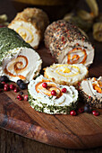 A delicious selection of flavoured cheese rolls, garnished with herbs, apricots, berries and nuts, presented on a rustic wooden board.