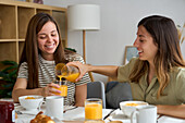 Ein glückliches lesbisches Paar frühstückt zu Hause und genießt die Gesellschaft des anderen Orangensaft, Croissants und Lachen schaffen einen fröhlichen, intimen Moment