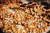 A tempting display of colourful waffles covered in marshmallows, nuts and chocolate icing, with various pastries behind them to complement the attractive shop window of a patisserie
