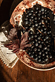 A rustic autumn still life with fresh blueberries on a decorative vintage plate. A dry maple leaf and a lace doily add a cosy, nostalgic touch to the wooden table.