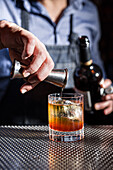 A bartender skilfully pours an ingredient into a whiskey old fashioned, capturing the art of mixology The focus is on the preparation of the drink