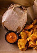 A wrapped burger from Madrid with crispy potato wedges and a flavoursome dipping sauce. The aesthetic presentation emphasises a delicious fast-food meal that can be enjoyed immediately.