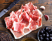 Thinly sliced prosciutto on a wooden board, accompanied by black olives and a bowl of olive oil. A rustic ambience emphasises the gourmet appeal.