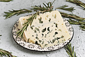 A slice of blue cheese with fresh rosemary lies on a patterned plate and creates a delightful combination of flavour and appearance, perfect for gourmet presentations.