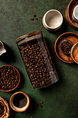 A cosy scene with coffee beans in a glass jar, surrounded by ceramic cups and wooden bowls on a textured green surface - perfect for a rustic coffee-themed design