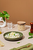 Ein schön angerichtetes Nudelgericht, garniert mit geriebenem Parmesan und frischem Basilikum, auf einem stilvollen Tisch mit einem Glas Wasser, einem Glas mit trockenen Nudeln und eleganten Essensaccessoires