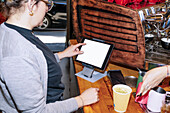 A customer navigates through a digital menu on a tablet in a café. A barista prepares a speciality coffee, highlighting the combination of tradition and technology in modern coffee culture.