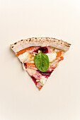 Top view of a delicious slice of pizza with beetroot, creamy sauce, mozzarella and a fresh basil leaf, presented on a plain background.