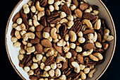 Top view of a ceramic bowl filled with a mixture of different nuts, including almonds, pecans, hazelnuts and cashews The different textures and rich colours emphasise the natural goodness