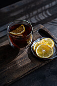 A clear glass filled with amber-coloured tea with fresh lemon slices against a rustic wooden background is reminiscent of a cosy, traditional English teatime.