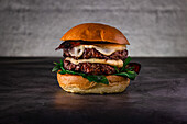 Close-up of a delicious cheeseburger with melted cheese, crispy bacon and fresh greens, all nestled in a soft bun. The rustic table decoration emphasises the attractiveness of the dish.