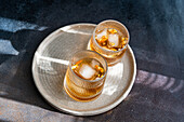 Top view of two spiced cognac cocktails with cinnamon and star anise, served on a textured ceramic plate, accompanied by almonds, peanuts and walnuts.