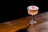 A sophisticated pisco sour cocktail on a wooden surface that showcases its frothy lace and delicate colour tones - perfect for adding a touch of elegance to any occasion with a classic cocktail