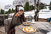 A person photographs their meal at the Geisleralm, a picturesque mountain hut restaurant in the Dolomites, Italy Snow-capped mountains and rustic wooden tables form the backdrop