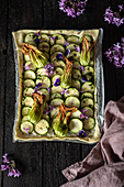 A beautifully arranged courgette cake with edible flowers on a rustic wooden table. The bright colours and textures make it an eye-catching culinary masterpiece.