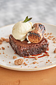 Ein reichhaltiger Schokoladen-Brownie, garniert mit cremigem Vanilleeis und gerösteten Marshmallows, garniert mit Minze, zerbröselten Keksen und Karamellspritzern