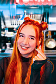 A smiling woman with bright red-orange hair at an Asian food market She gestures enthusiastically amidst the market lights, capturing the vibrant and cultural surroundings