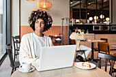 A young professional with vitiligo works on a laptop in a stylish, modern café. Soft natural light pours in through large windows, creating an inviting atmosphere for productivity and relaxation