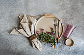 An elegantly laid table with a ceramic plate, fork and knife and a bouquet of pink flowers A beige napkin and a purple glass lend the scene a rustic autumn charm