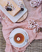 A delicate Swiss roll with a creamy dulce de leche filling is presented next to a cup of tea, accentuated by cherry blossoms and pastel-coloured textiles.