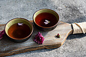 Two ceramic cups filled with herbal tea, each garnished with purple petals, stand on a rustic wooden board The scene conveys a sense of calm and natural beauty