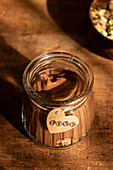 A warm, sunlit shot of vegan chocolate mousse in a clear glass, decorated with a heart-shaped love tag, against a rustic wooden backdrop.