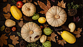 An arrangement of pumpkins, pine cones and autumn leaves on a dark wooden background, representing the abundance and colours of autumn. Ideal for seasonal themes.