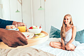 A tray with a selection of fresh fruit, orange juice and breakfast items is served to a person resting in bed. The scene radiates comfort and a peaceful morning mood.