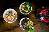 Top view of three gourmet bowls, broccoli and cauliflower in satay sauce, chicken with glass noodles and peanuts and roasted beef with fresh greens, pear slices and sesame seeds