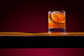 A sophisticated old-fashioned whiskey cocktail, garnished with a slice of orange on a wooden bar The rich amber tones and elegant presentation convey a classic and timeless feel