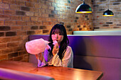 Asian Gen Z girl enjoys pink candy floss Warm ambient lighting and brick walls create a relaxed and stylish atmosphere