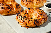 A close-up of golden brown bagels sprinkled with black sesame seeds resting on a white marble slab. Perfect for breakfast scenes, bakery adverts and culinary blogs.