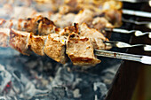 Nahaufnahme von saftigen, stückigen Spießen, die auf einem rauchigen Grill auf einem belebten Straßenfest brutzeln und die köstliche Kunst der Essenszubereitung im Freien demonstrieren.