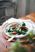 A healthy dish with fresh spinach leaves, crisp apple slices and crunchy pecans, garnished with sesame seeds and served on a white plate.