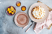 A homemade lemon cake with citrus slices is placed on a plate on a rustic table. The arrangement includes empty plates, two glasses filled with orange juice and cutlery.
