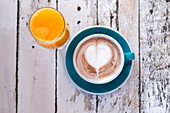 A cosy scene with a cup of cappuccino with heart-shaped latte, paired with a glass of fresh orange juice, on a rustic wooden table.