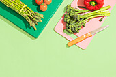 A colourful assortment of vegetables, including asparagus, cherry tomatoes and broccoli, lies on colourful chopping boards. A knife with a wooden handle lies next to it. Perfect for healthy cooking themes.