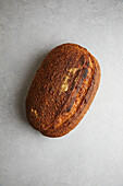 Top view of a freshly baked sourdough bread with a crispy crust and golden hue, perfectly structured and resting on a textured grey background.