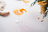Elegant tangerine cocktail, served in a stemmed glass, garnished with an orange zest, on a textured white tablecloth. The subtle lighting emphasises the calming ambience, which is perfect for a refreshing moment.