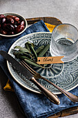 A tasteful arrangement of Greek grilled olives on a ceramic plate, accompanied by a glass, rustic utensils and textured bed linen. The scene captures a balance of elegance and tradition and is perfect for culinary themes.