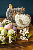 Decorative Easter set-up with pastel-coloured eggs, woollen chicken figurines and delicate white flowers on a wooden table, perfect for seasonal celebrations.