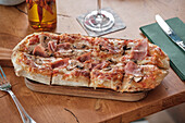Herzhafte Fladenbrotpizza mit Schinkenscheiben, Pilzen und geschmolzenem Käse, serviert auf einem Holzbrett, perfekt als Snack oder leichte Mahlzeit