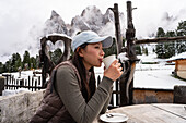 A woman enjoys a warm drink on the Geisleralm in the picturesque Dolomites Snow-capped mountains and rustic wooden decorations create a cheerful Alpine ambience
