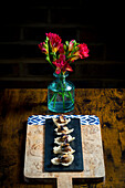 Elegant cracker canapes with vegetable satay and peanuts, served on a black slate platter on a wooden board A vase of red flowers adds a lively touch to the rustic arrangement