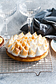 A beautifully baked, homemade lemon cake with toasted peaks rests on a cooling rack. Crystal glasses and linen napkins create an elegant dessert decoration.
