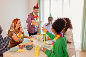 A cheerful birthday party with friends gathered around a table. Everyone is wearing party hats and wreaths of flowers, enjoying food and drink and creating a cheerful atmosphere.