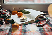 A Christmassy ambience with a burning candle on an open book, surrounded by oranges and fairy lights that radiate warmth and a Christmassy atmosphere.