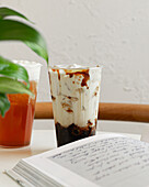 Close-up of two refreshing iced drinks on a table, one with milk tea and the other possibly with fruit tea An open notebook and a green plant create a relaxed, inviting atmosphere