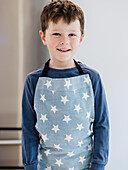 A smiling boy in a blue, star-patterned apron, ready for a fun kitchen activity. The bright and playful atmosphere emphasises creativity and joy.